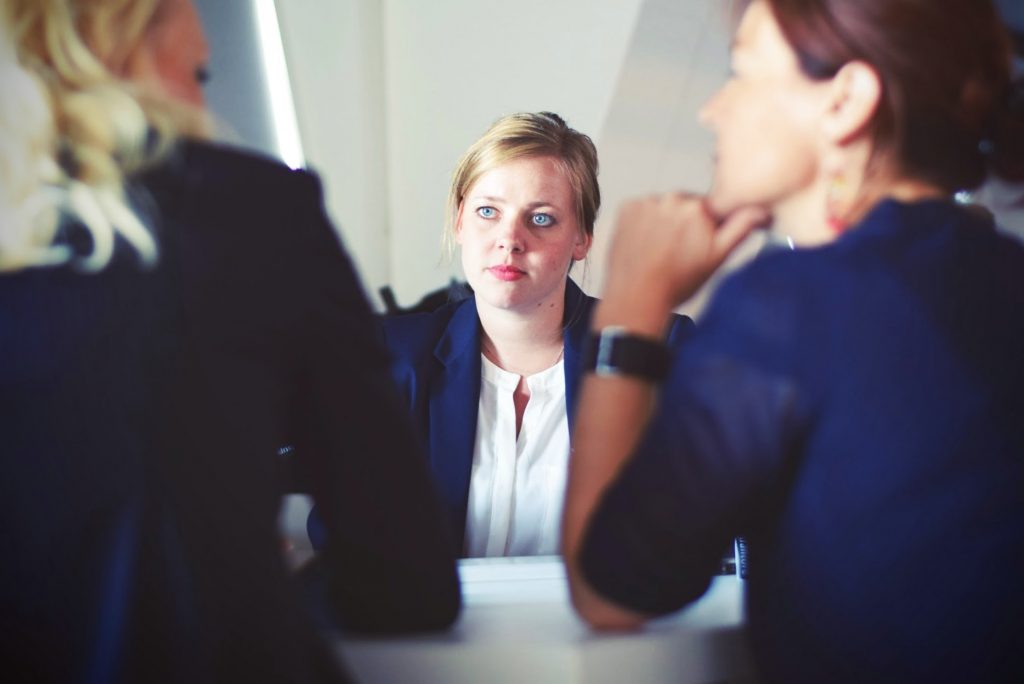 A woman in an interview being asked "Do you have any questions for us?" (Photo by Tim Gouw from pexels.com)