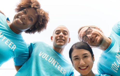 A group of four young adults wearing blue t-shirts that say "VOLUNTEER."