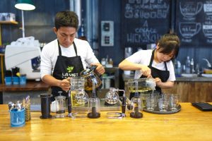 Two baristas making complex coffee drinks, in an example of a job that is often overlooked when considering what to include on a college graduate resume.