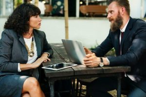 A photo of two businesspeople in a meeting. One is making a firm point while the other listens and considers attentively.