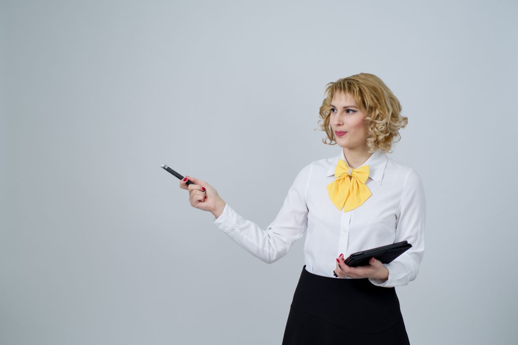 A photo of a businesswoman holding a clipboard and gesturing with a pen to show something offscreen.