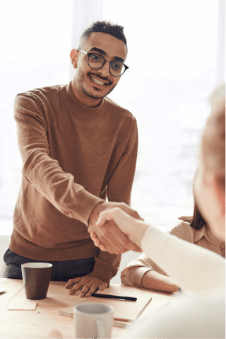 A photo of a man in a brown sweater shaking the hand of a seated woman, presumably as a professional connection.