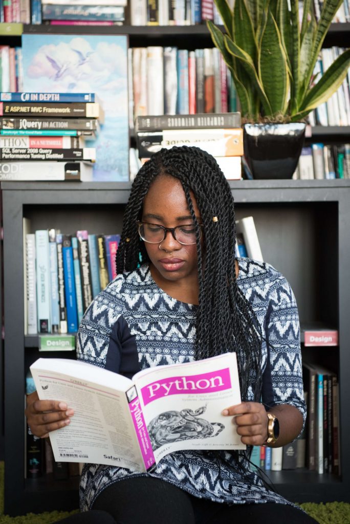 An image of a female student in a library reading a book on Python, demonstrating academic learning, a example of relevant experience that can be on a career change resume.