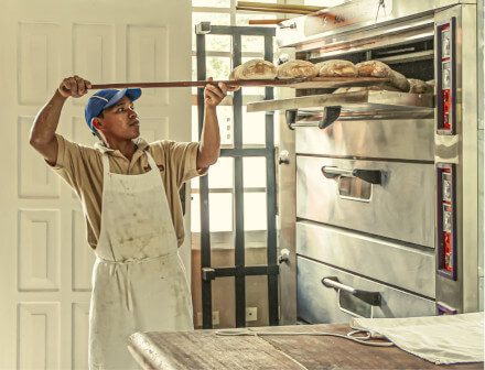 An image of a man in a bakery with an apron putting food into an oven, representative of the fact that only relevant information should go in a resume certifications section.