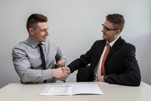 A photo of two men smiling and shaking hands.