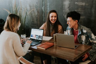 A photo of three young people on laptops doing schoolwork together at a table. Article on cover letter for internship