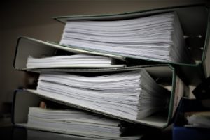 A stack of binders with large quantities of paper in them, symbolizing the amount of resumes a recruiter would have to manually search through without using ATS in recruitment.