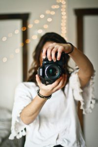 A woman pointing a DSLR camera towards the viewer, representing the point that one should not include a photo on a resume in 2020, no matter how professional it looks.