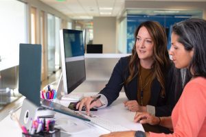 A photo of a businesswoman working with another woman, both looking at the same screen, used to illustrate the nature of working with an external recruiter (vs an internal recruiter with a different job function. (Photo courtesy of LinkedIn Sales Navigator.)