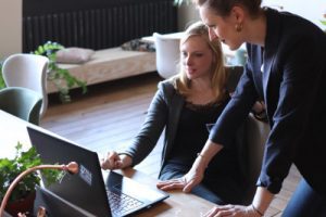 A stock photo of one professional woman showing another work done on a computer, demonstrating  collaborative brand of leadership style. Photo by CoWomen on Unsplash.