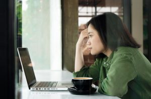 A photo of a woman looking at a laptop intently with a cup of coffee in front of her, illustrating the in-depth research needed to make a pain letter work.