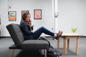 A stock photo of a woman sitting on a couch having a phone call, illustrating the importance of following up about salary if it was not mentioned in the job description.