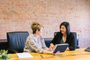 A stock photo of two professionally dressed women discussing a document on a tablet. (Photo by Amy Hirschi on Unsplash.)