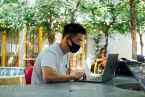 person in mask on computer. Photo by Paul Hanaoka on Unsplash