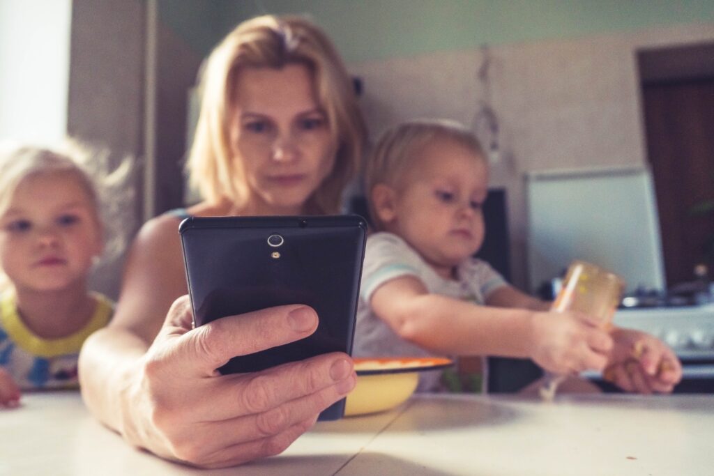 woman on a phone holding two kids 